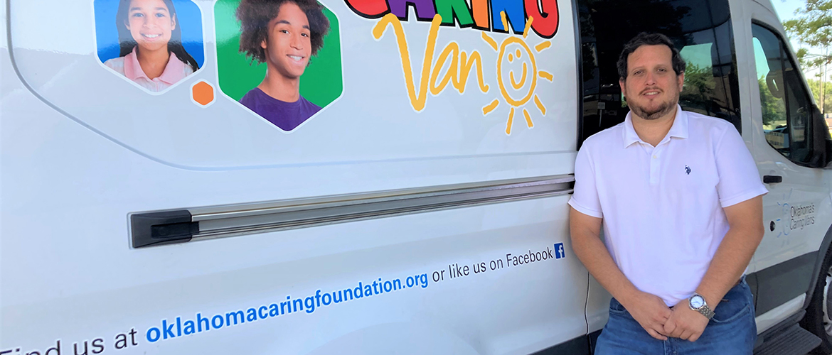 A man stands next to a white van painted with Caring Van in colorful letters 